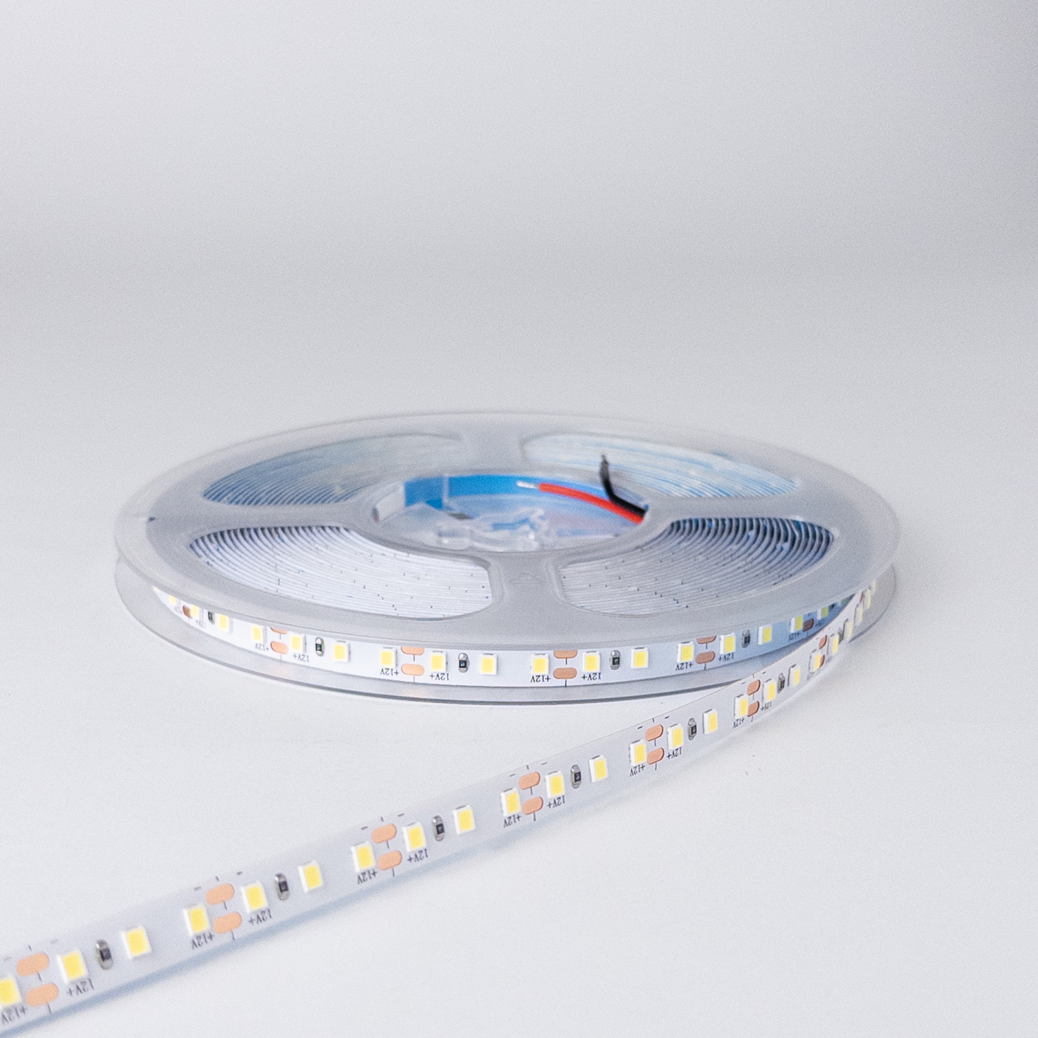 LED traka 12V 6000K 10W hladno bela, ugašena na providnom koturu, sa natpisima +12V pored bakarnih polja