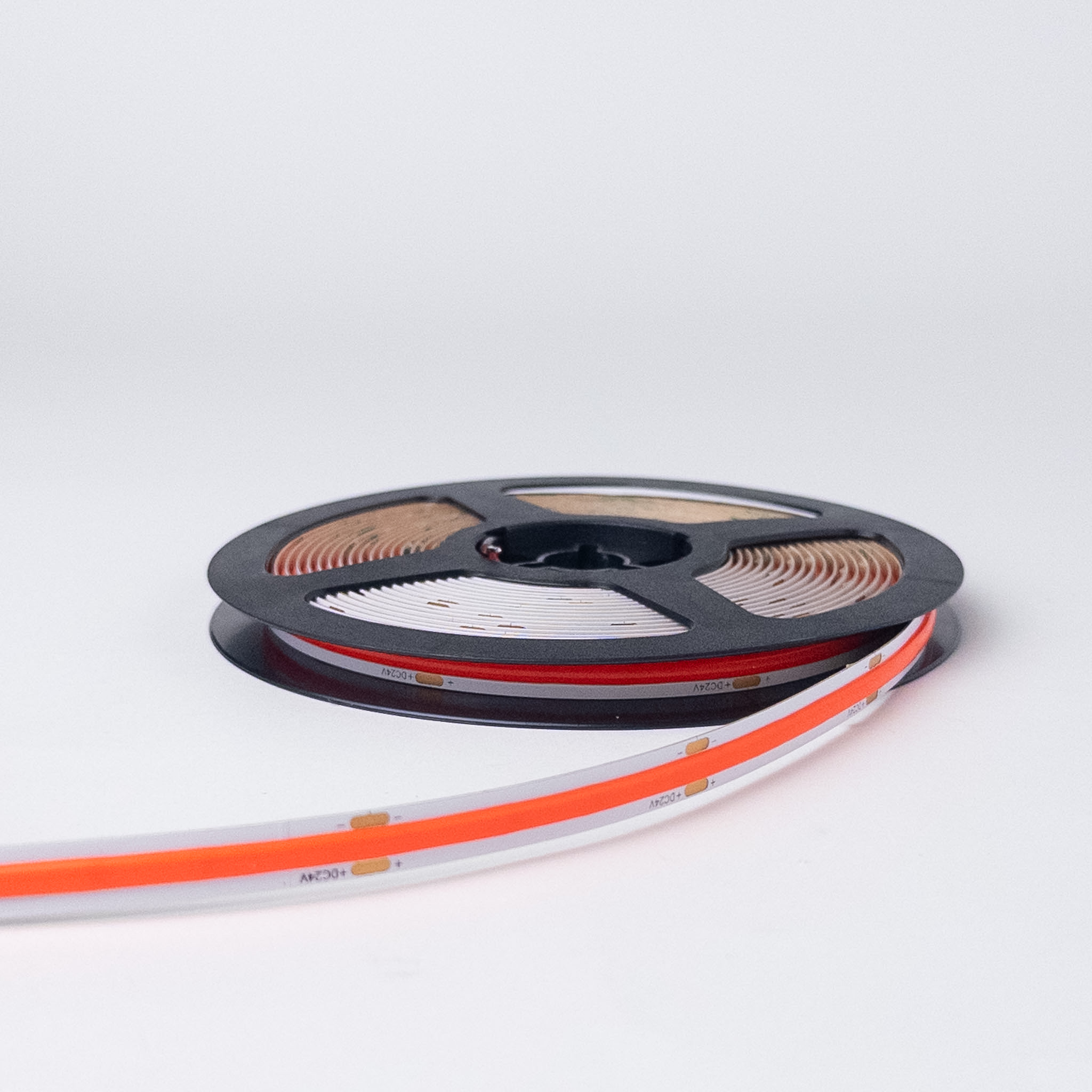 Crvena COB LED traka 24V na crnom koturu pre paljenja, sa crvenonarandžastim slojem i natpisom +DC24V uz bakarna polja